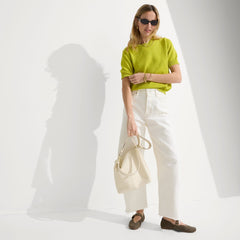 The Mini Zip Bucket in White Sand worn as a crossbody by a female model, shown in motion from the right.