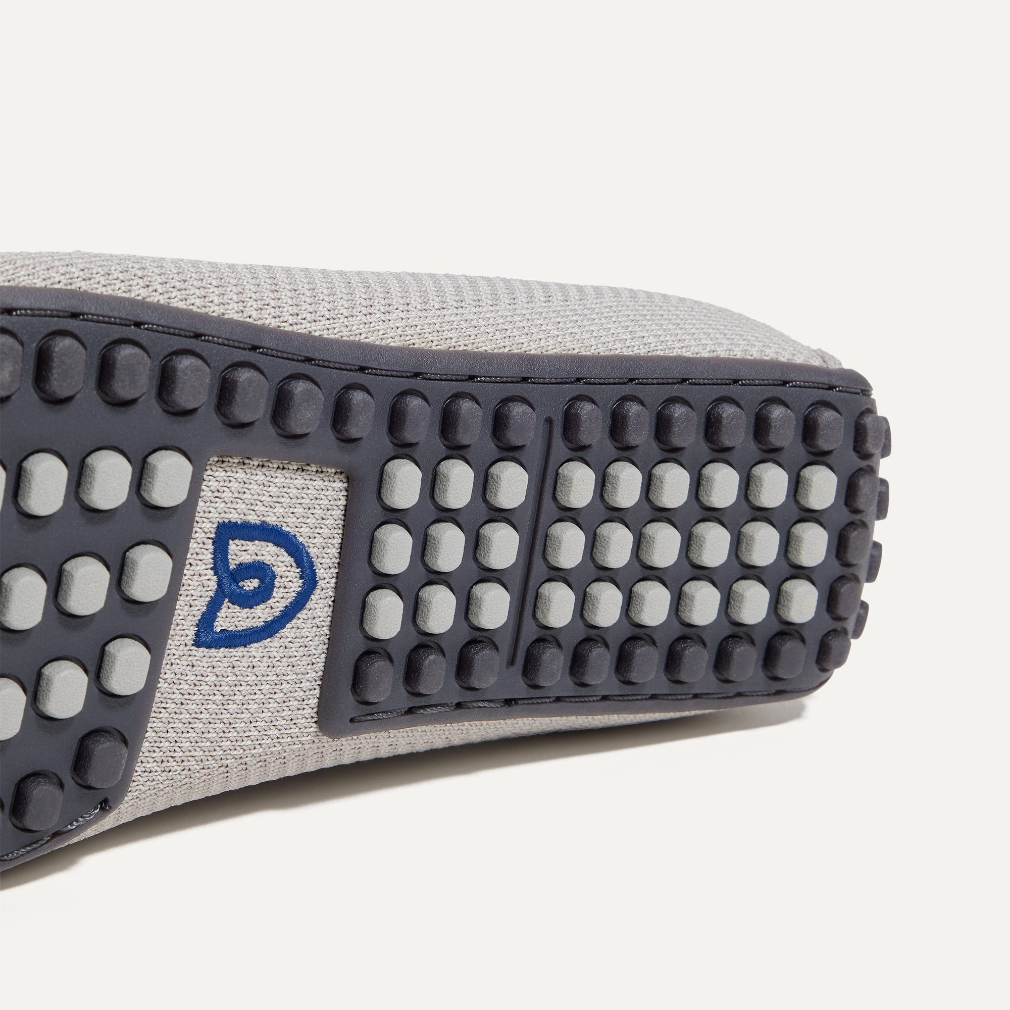 Close up of the outsoles of The Driving Loafer in Light Grey Herringbone, with raised nub details and the Rothy's signet on the base of the shoe. 