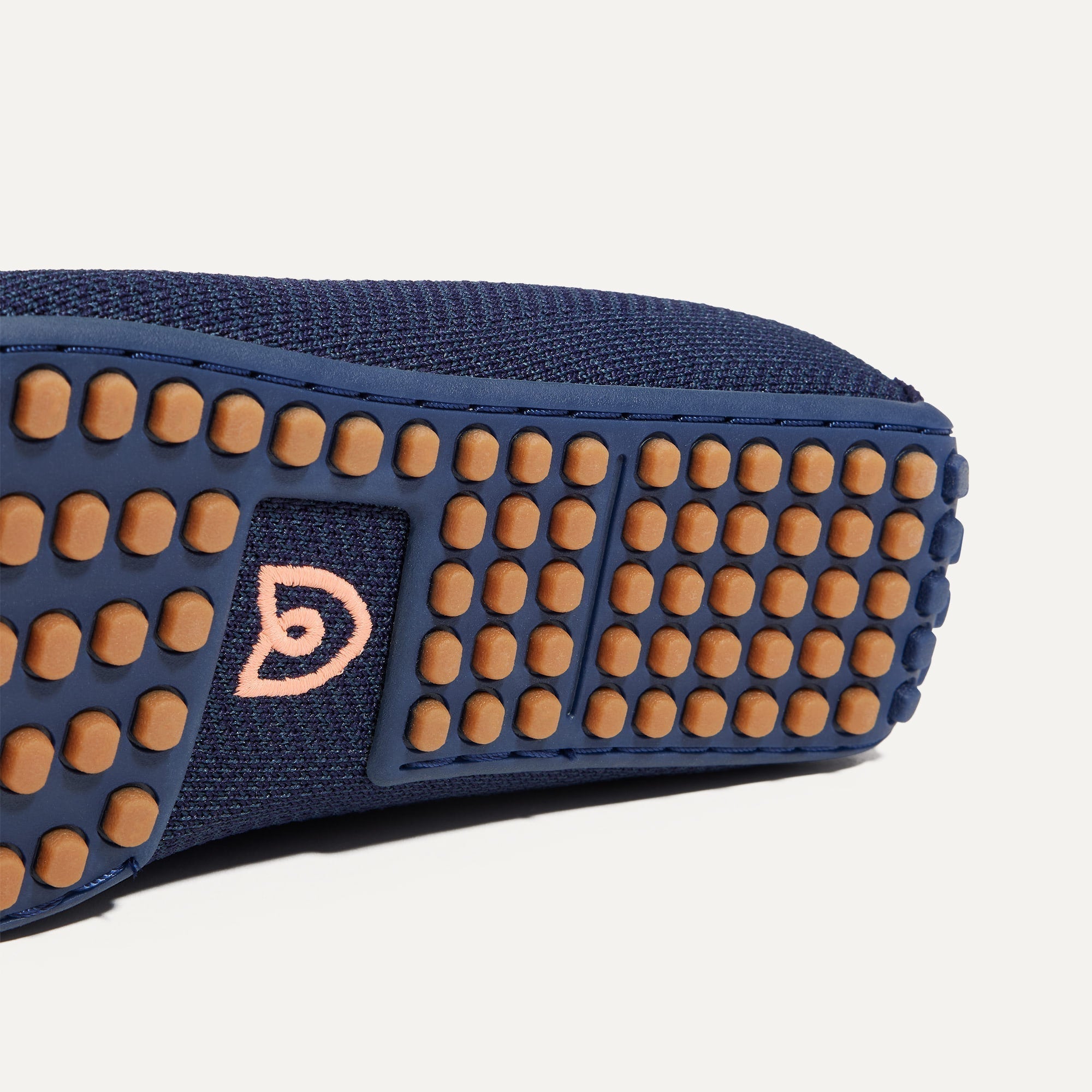 Close up of the outsoles of The Driving Loafer in Navy Herringbone, with raised nub details and the Rothy's signet on the base of the shoe. 