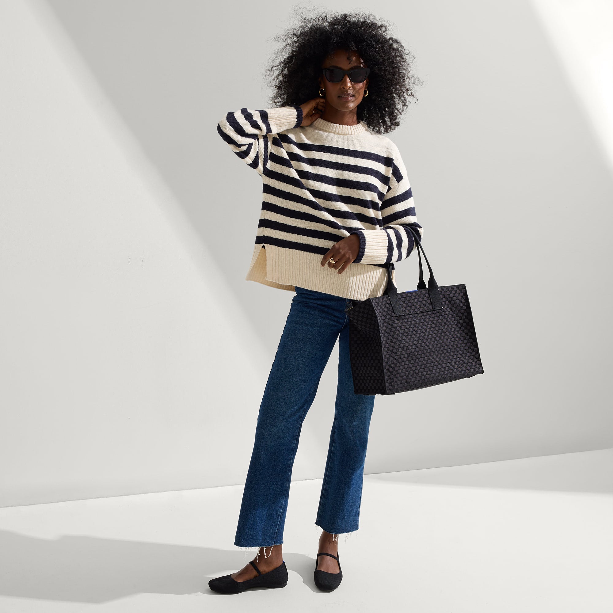 The Classic Tote in Black Sand, carried by its top handles by a model, shown from front.