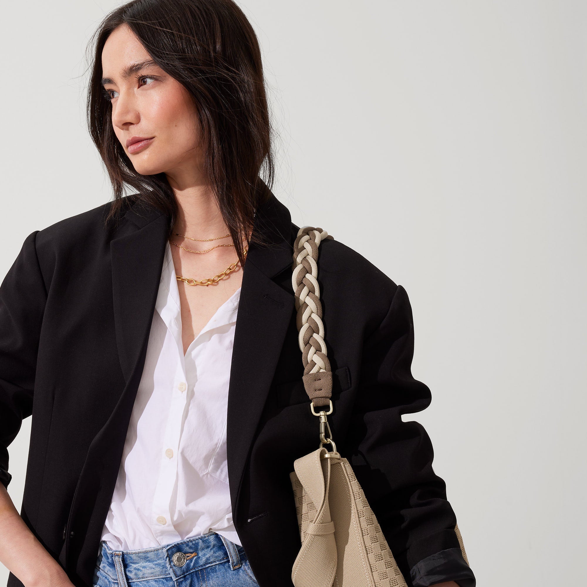 An alternate image of The Braided Shoulder Strap in Cream & Cocoa, shown paired with The Bucket Bag and held by a model. 