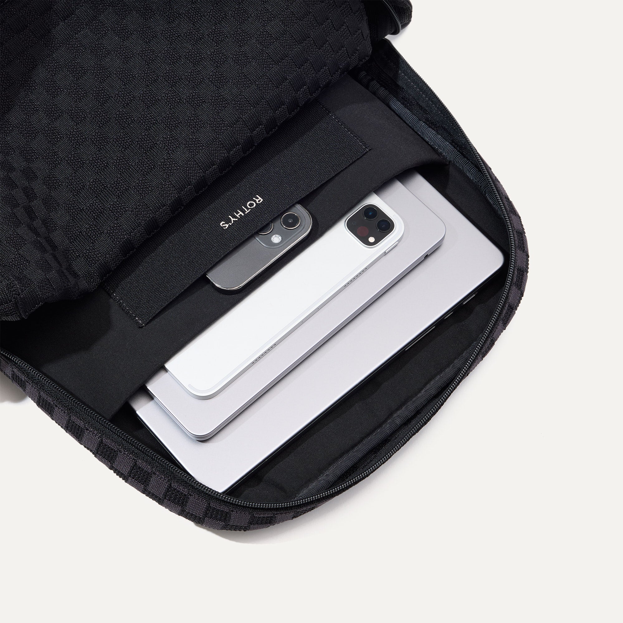 A close up of The Backpack in Black Sand showing the interior pockets with a laptop, tablets and a phone inside.