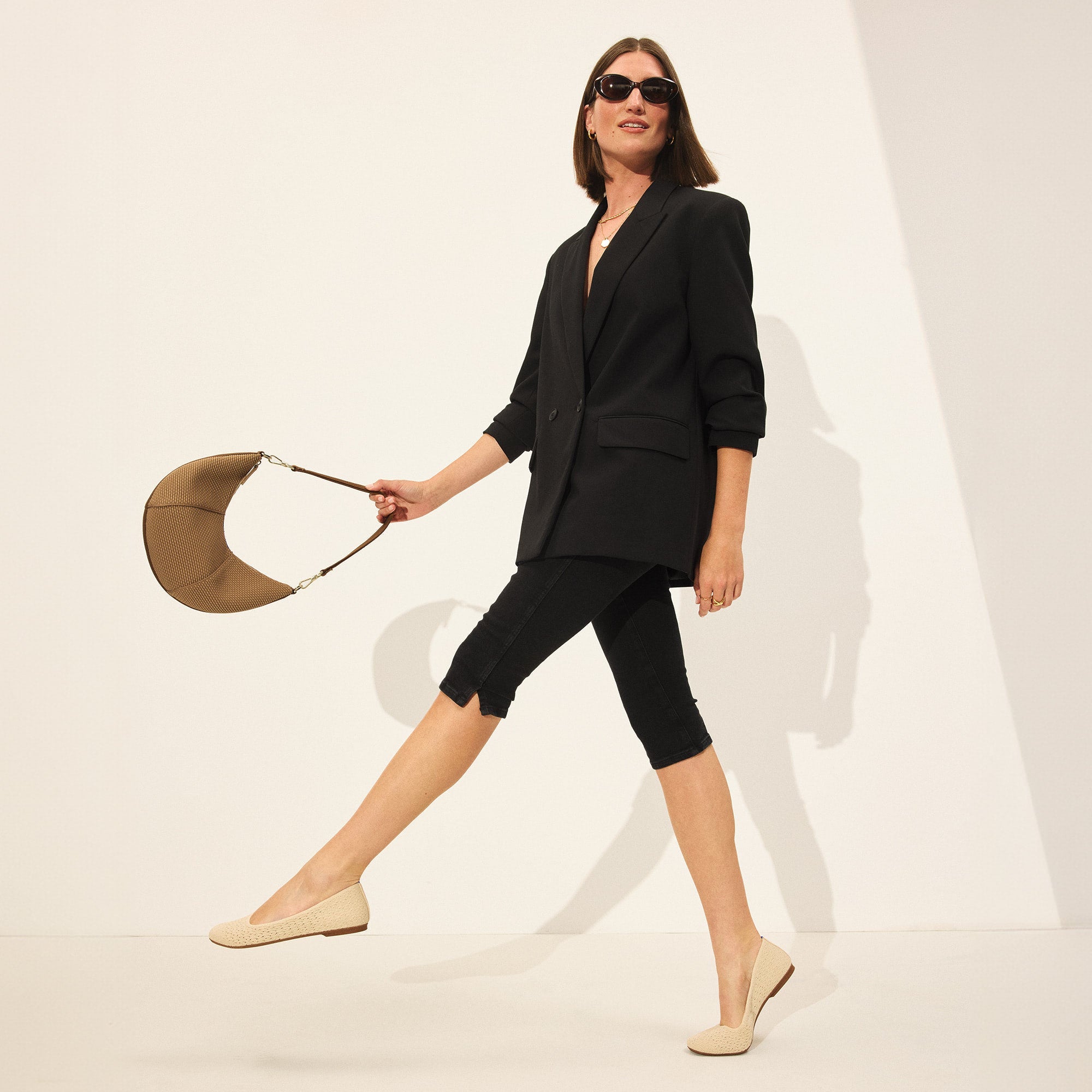 Another view of model holding The Crescent Bag in Horizon by the shoulder strap, shown in motion.