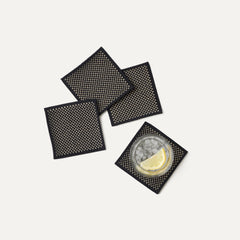 A set of four Coasters in Peppercorn shown with a drink.