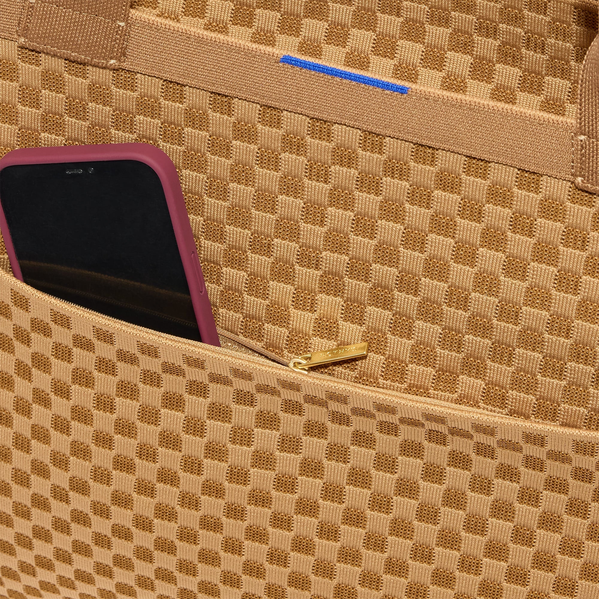 A close up of The Zip Travel Tote in Hazelnut with a phone slipped into the outer pocket.