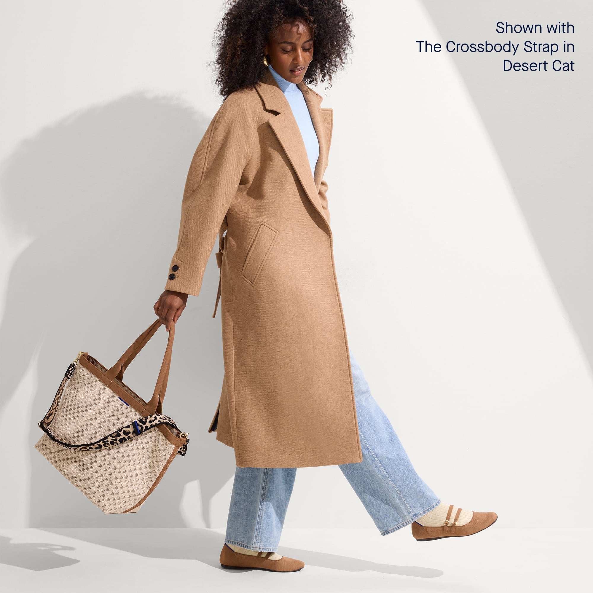 An alternate view of a model holding The Lightweight Zip Tote in Vanilla Wafer paired with The Crossbody Strap in Desert Cat.